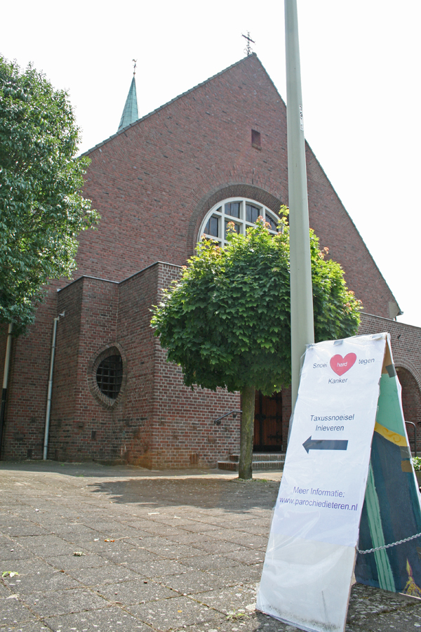De kerk met op de voorgrond het bord met de campagne “Snoei hard tegen Kanker”.